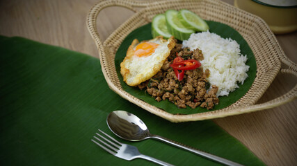 Thai traditional food, Stir fried minced pork with basil (Pad ka prao), rice fried egg serving on wicker plate and silverware