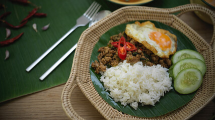 Stir fried minced pork with basil (Pad ka prao), rice fried egg serving on wicker plate and silverware