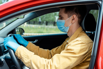 driver in medical mask and protective gloves holding steering wheel in car during covid-19 pandemic