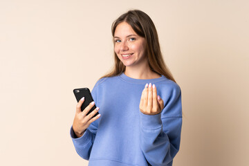 Young Lithuanian woman using mobile phone isolated on beige background inviting to come with hand. Happy that you came