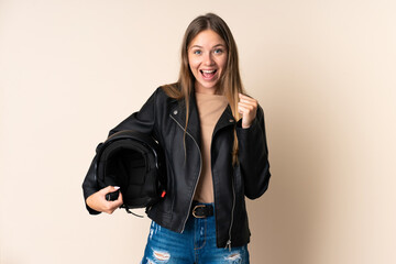 Young Lithuanian woman holding a motorcycle helmet isolated on beige background celebrating a victory in winner position