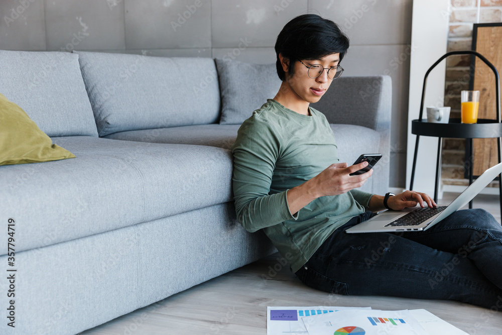 Wall mural image of serious asian man working with laptop and cellphone