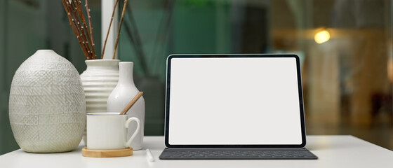 Blank screen digital tablet on modern home office desk with cup and ceramic decorations