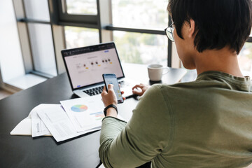 Image of serious asian man working with laptop and cellphone