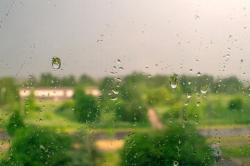 Raindrops on a window with green trees and a cloudy sky in the background on a summer day