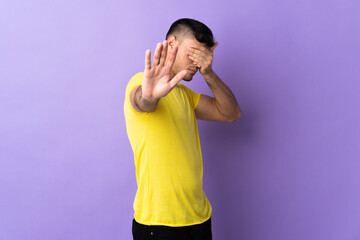 Young Colombian man isolated on purple background making stop gesture and covering face