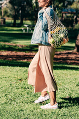 A woman who do groceries with a mesh reusable cotton bag.  The tote is full vegetables and fruits because she is vegan and mindful about environment