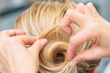 Close up rear view of hairdresser making hairstyle for long hair of blonde woman.