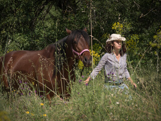 Female rider wearing a western hat and her andalusian mare walking in the countryside.