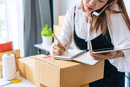 Busy Business Owner Multitasking With Talking On The Phone With Customer, Take Note On Notebook And Checking Stock Balance From Tablet. Online Selling, E-commerce, Shipping, New Normal Concept