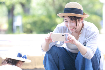 砂場で遊ぶ子供をスマートフォンで撮影する母親