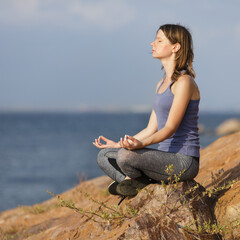 Woman meditating on the coastline. Healthy lifestyle concept, sport training on summertime.