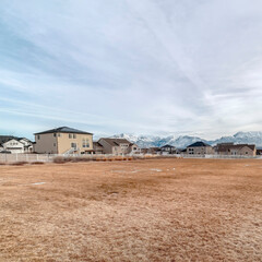Square crop Grassy field with melting snow against homes and snowy mountain background