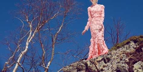 A beautiful young girl stands in the mountains in the spring, trees, rocks, blue sky, sunny weather, in a fashionable luxurious pink lace-fitting dress