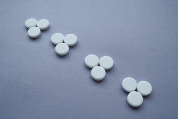 Round medicinal pills in the form of triangles arranged in a row on a dark purple background,...