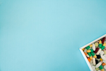 multi-colored pills and capsules in the box, different pills located in the lower right corner on a blue background, with free space for text, isolated