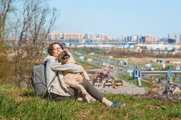 Happy Girl and Labrador Retriever hug and laugh while sitting on a mountain. Vacation with a dog in the city