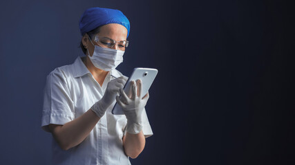 Fototapeta na wymiar Doctor working with database on digital tablet. Caucasian woman in mask and gloves uses digital gadget standing on blue gray background with copy space for text on right side. Tinted image.