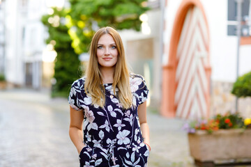 Beautiful young woman with long hairs in summer dress going for a walk in German city. Happy girl enjoying walking in cute small fachwerk town with old houses in Germany.