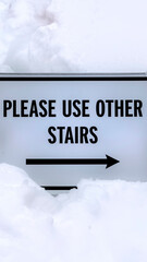 Vertical Sign that reads Please Use Other Stairs against fresh white snow in winter