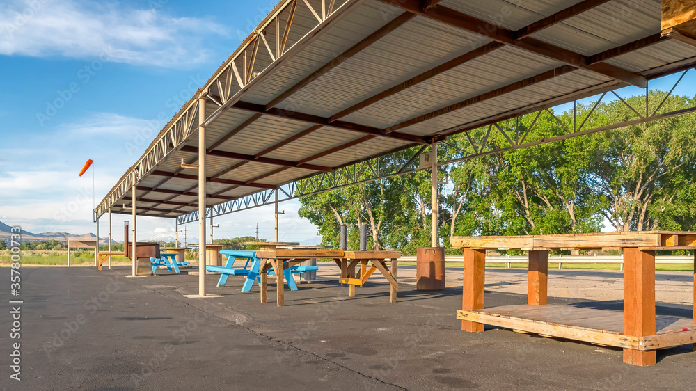 Wall mural Panorama Tables and benches under flat corrugated metal roof of a pavilion at a park