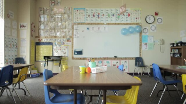 Empty elementary school classroom with white board, table and chairs, slider shot.