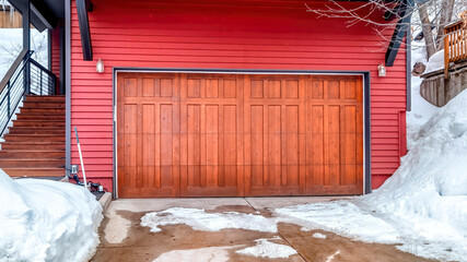 Fototapeta na wymiar Panorama frame Brown garage door and red wall of home with snowy yard and driveway in winter