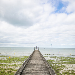 wooden pier on the beach with a man standing and algae