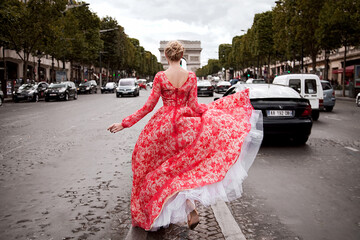 A beautiful young woman runs in a luxurious peach long dress on the middle of the road in Paris,...