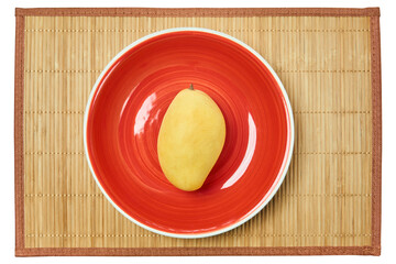 yellow mango on a red plate on a cane place mat