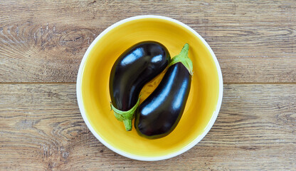 two dark violet eggplants on a yellow plate on a wooden tabletop