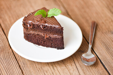 Cake chocolate delicious dessert served on the wooden table - cake slice on white plate with topping chocolate and mint leaf