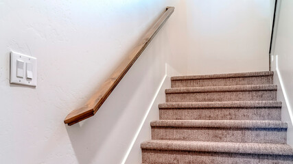 Panorama Carpeted indoor staircase of home with brown handrail against white side wall