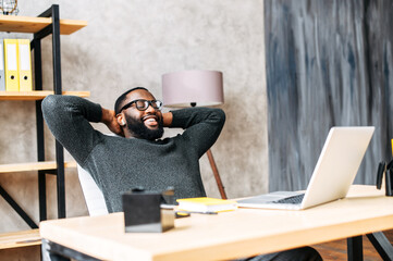Take a break on a workplace. A young African-American guy leaned back in his chair relaxed, he is...