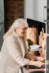 Fototapeta na wymiar smiling elderly woman washing vegetables on kitchen