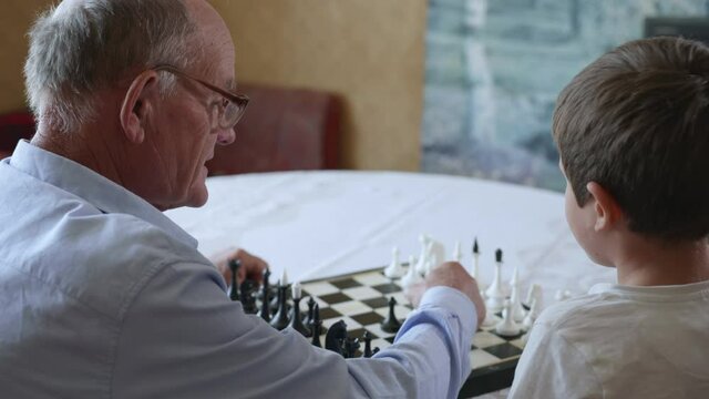 intellectual games, old grandfather plays with his smart child playing board games of chess sitting at table in room