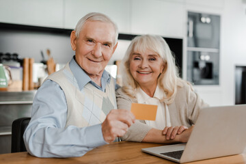 happy senior couple shopping online with credit card and laptop at home during quarantine