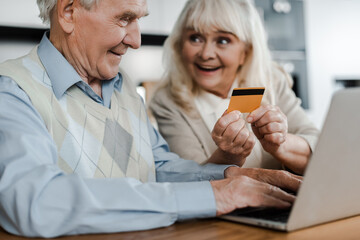 excited senior couple shopping online with credit card and laptop at home during self isolation