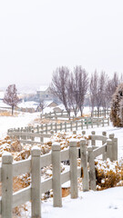 Vertical crop Low wooden picket fence winding through a snow covered grassy terrain in winter