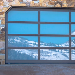 Fototapeta na wymiar Square frame Garage door with glass panes reflecting a snowy hill landscape under blue sky