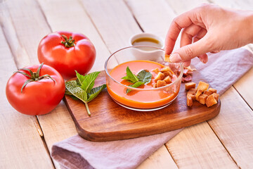 Women's hands throwing pieces of bread in to a plate of gazpacho. Mediterranean food and healthy diet.