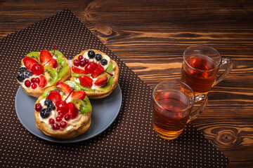 Home made cake with cream and fruit and hot tea on wooden table.