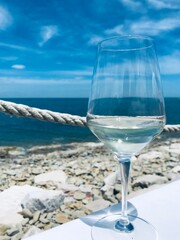 Close up of an almost empty glass of white wine on the table of a sea front restaurant, with amazing sea view in the background. fine dining experience.