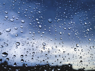 Rain drops on the window glass as background with copyspace for your text, with silhouette of some buildings and dark thunderstorms sky behind the window on rainy day. Selective focus