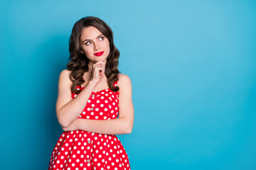 Photo of attractive curly lady minded good mood arms crossed look up empty space interested creative person arm on chin wear red dotted retro dress isolated blue color background