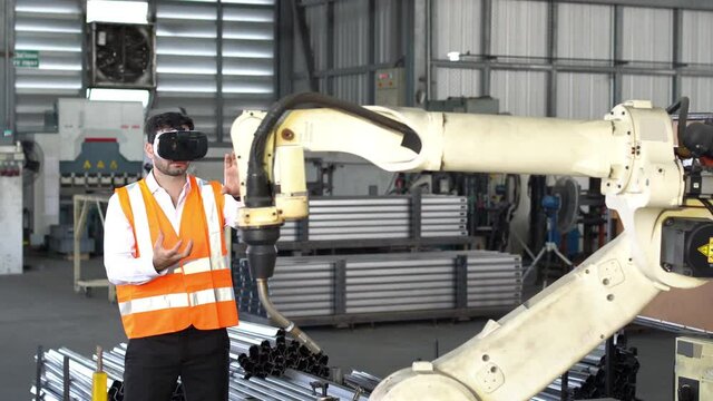 Engineer in virtual 3D reality headset controlling robot at factory.