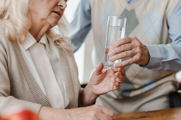cropped view of elderly husband and ill wife with glass of water at home during quarantine