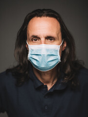 Portrait of an adult male in a medical mask. The background is dark.