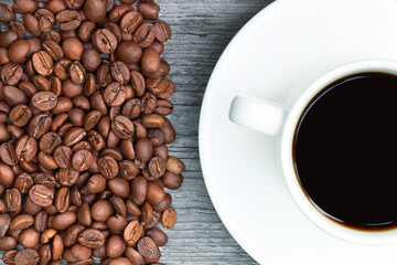 A cup of coffee and coffee beans on a wooden background. Heap of coffee beans. White coffee cup and saucer.Copy space. Place for text. Flat lay.