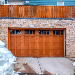 Square Brown wooden glass paned garage door against stone wall under balcony of home